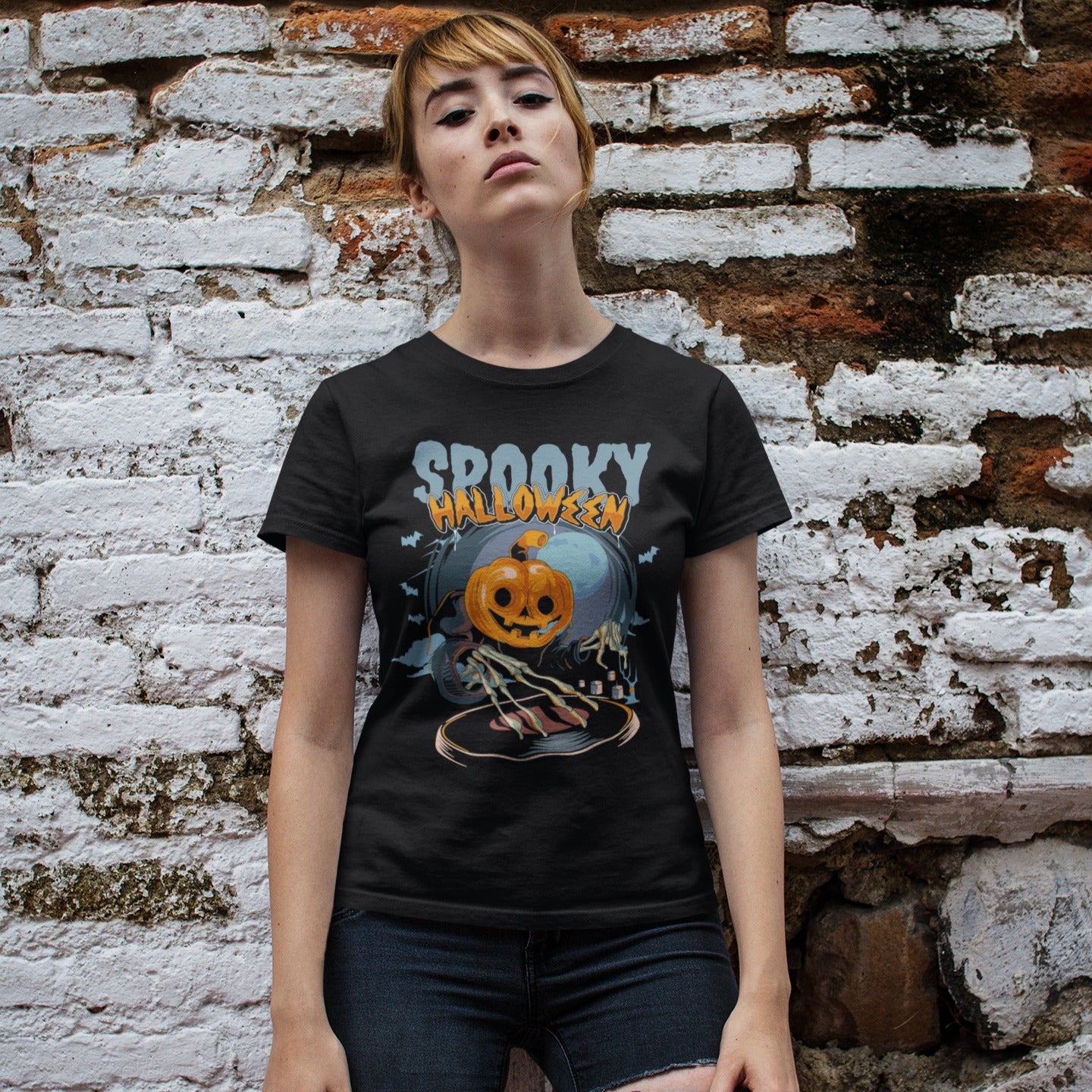 A black background features the distressed light blue text "SPOOKY" and distressed orange text "HALLOWEEN" with a white outline at the top. Below, a large, smiling jack-o'-lantern (pumpkin head) wearing a dark cloak is shown operating a DJ turntable. Skeletal hands with long fingers extend from the cloak over the turntable, manipulating it. In the background, there's a large, pale full moon, silhouetted bats flying, and cloud-like mist. The design represents a Halloween-themed DJ ready for a spooky music pa