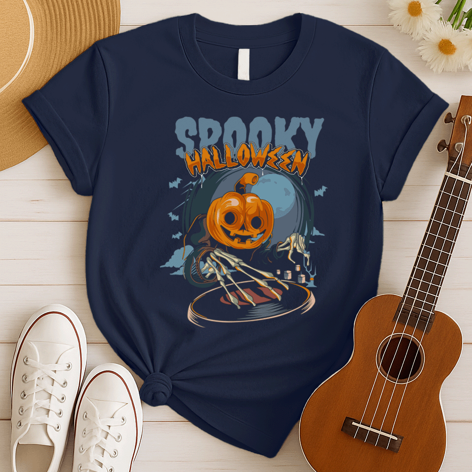 A black background features the distressed light blue text "SPOOKY" and distressed orange text "HALLOWEEN" with a white outline at the top. Below, a large, smiling jack-o'-lantern (pumpkin head) wearing a dark cloak is shown operating a DJ turntable. Skeletal hands with long fingers extend from the cloak over the turntable, manipulating it. In the background, there's a large, pale full moon, silhouetted bats flying, and cloud-like mist. The design represents a Halloween-themed DJ ready for a spooky music pa