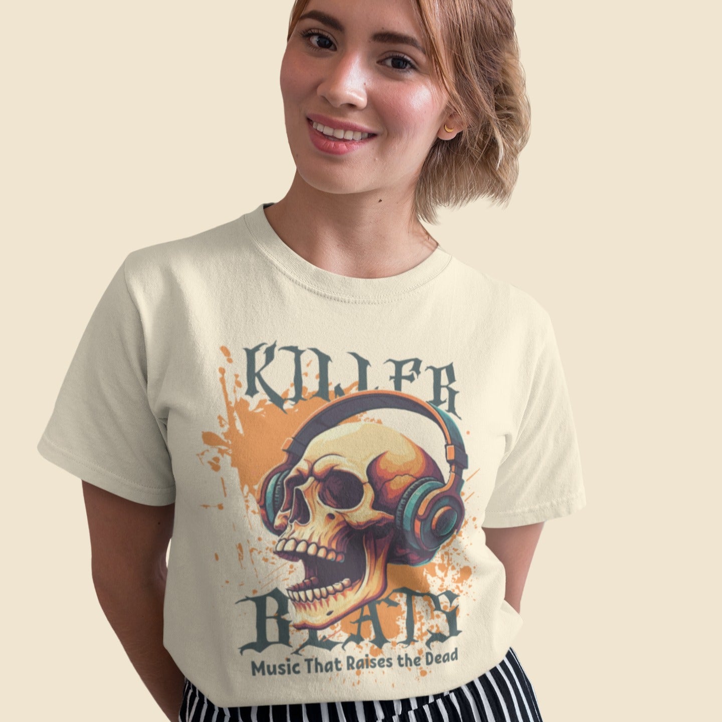 A light grey background with orange paint splatters features a stylized, detailed, orange and yellow human skull wearing large, teal and blue headphones. Distressed grey text above reads "KILLER" and below, "BEATS". Below that, smaller dark grey text says "Music That Raises the Dead". The design is a bold representation of music power and skull art.