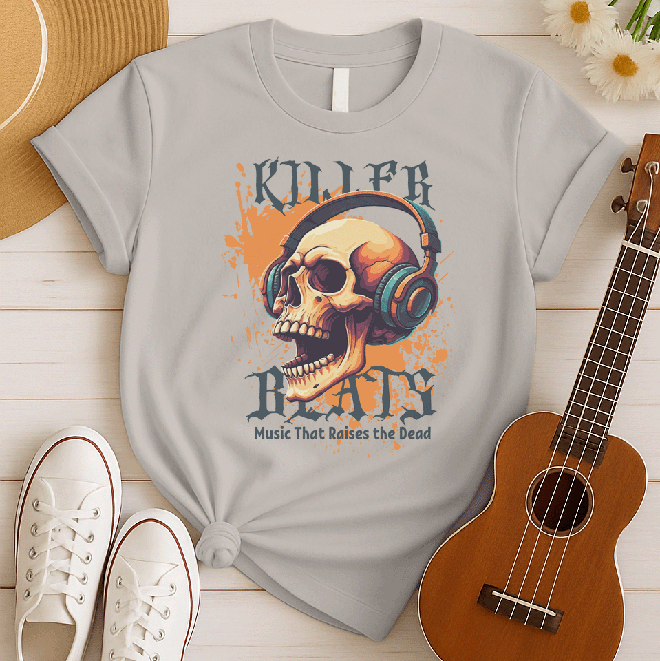 A light grey background with orange paint splatters features a stylized, detailed, orange and yellow human skull wearing large, teal and blue headphones. Distressed grey text above reads "KILLER" and below, "BEATS". Below that, smaller dark grey text says "Music That Raises the Dead". The design is a bold representation of music power and skull art.