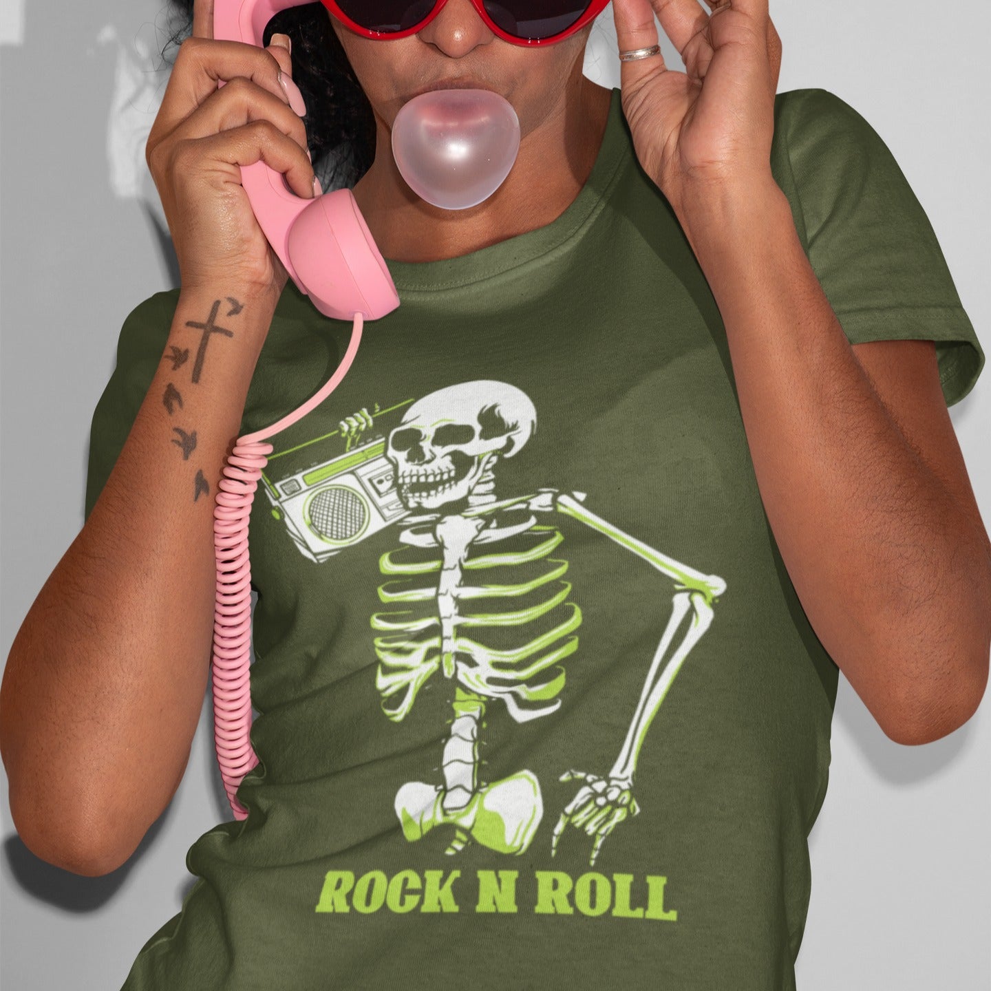 A striking graphic design features a full skeleton, rendered in white with a vibrant lime green glow on its bones, posed in a dynamic, walking stance. The skeleton holds a detailed, white outline of a retro boombox over its right shoulder. Below the skeleton, the bold, lime green text "ROCK N ROLL" is prominently displayed, creating a cool, energetic, and slightly spooky tribute to classic music.