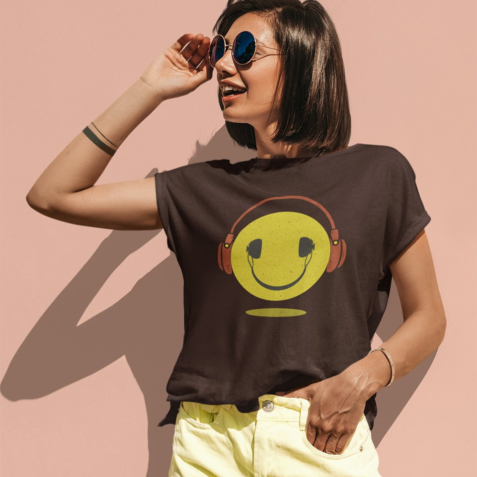 A bold and expressive graphic features a textured, distressed yellow smiley face with a prominent black smile and eyes. Large, rustic orange over-ear headphones, also with a distressed texture, are worn on top of the smiley face. The entire design creates a lively and vintage-inspired image that conveys happiness and a love for music.