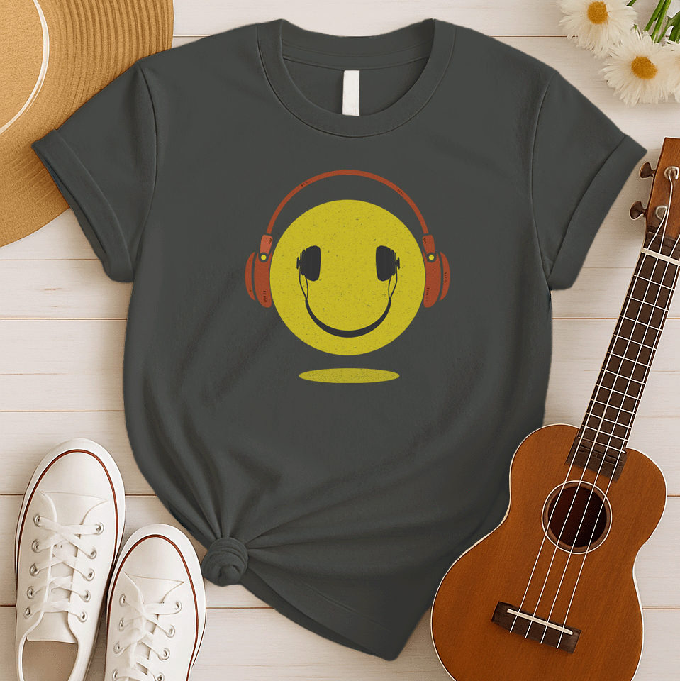 A bold and expressive graphic features a textured, distressed yellow smiley face with a prominent black smile and eyes. Large, rustic orange over-ear headphones, also with a distressed texture, are worn on top of the smiley face. The entire design creates a lively and vintage-inspired image that conveys happiness and a love for music.
