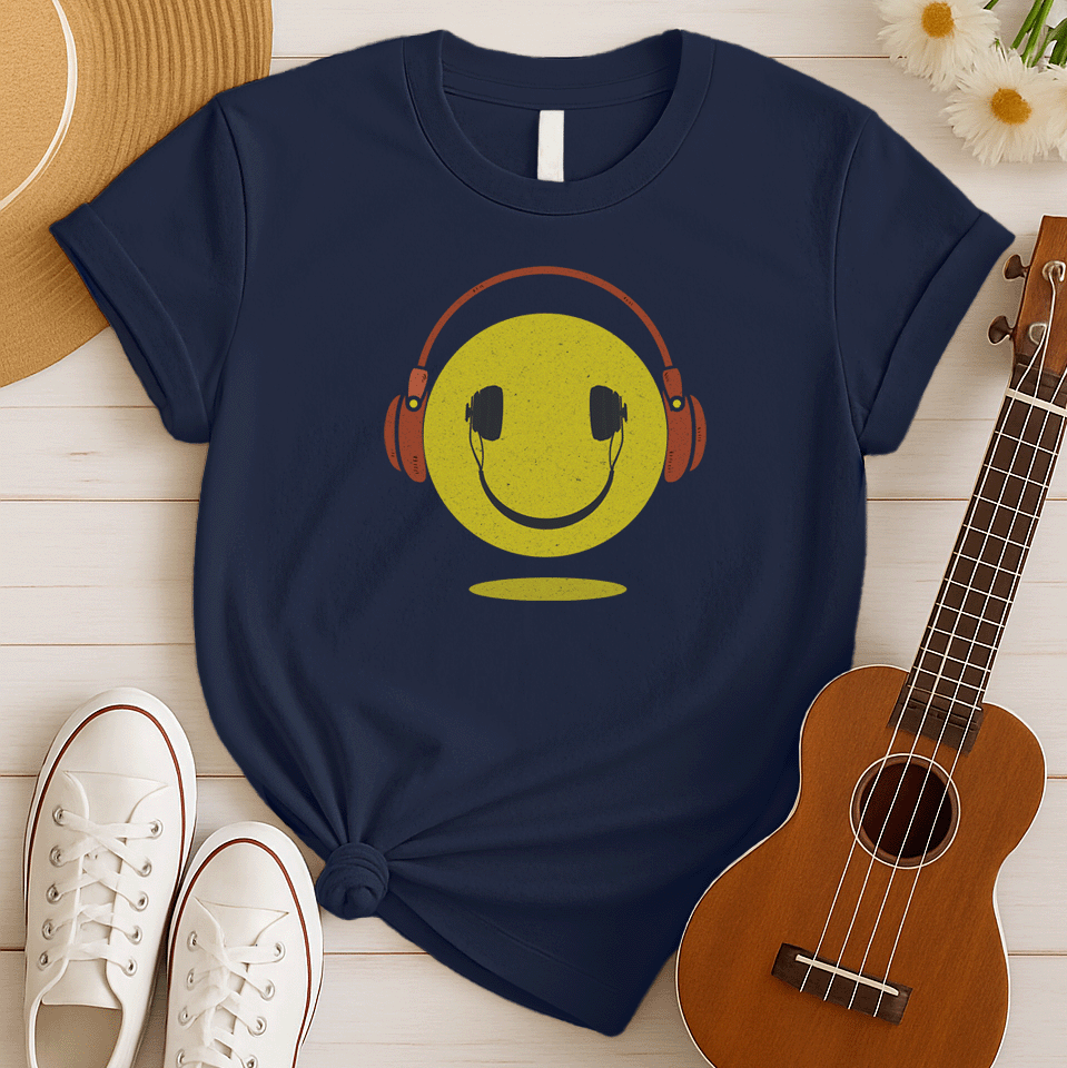 A bold and expressive graphic features a textured, distressed yellow smiley face with a prominent black smile and eyes. Large, rustic orange over-ear headphones, also with a distressed texture, are worn on top of the smiley face. The entire design creates a lively and vintage-inspired image that conveys happiness and a love for music.