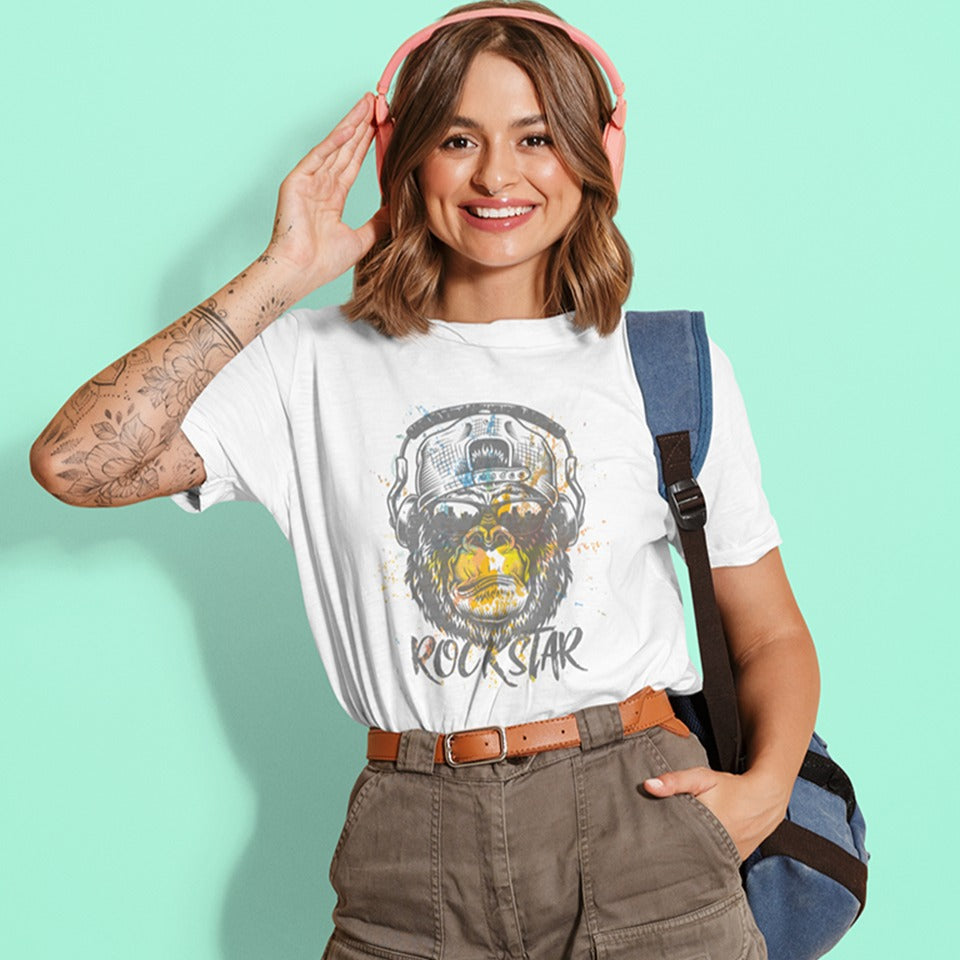 A grunge-style graphic features a detailed gorilla head wearing headphones, with the lower half of its face replaced by a textured splash of orange and yellow paint. The gorilla's fur and the headphones are rendered in shades of grey with distressed effects. Below the powerful primate, the word "ROCKSTAR" is emblazoned in a distressed white font with flecks of colorful paint matching the face. This striking design embodies raw power and musical rebellion.