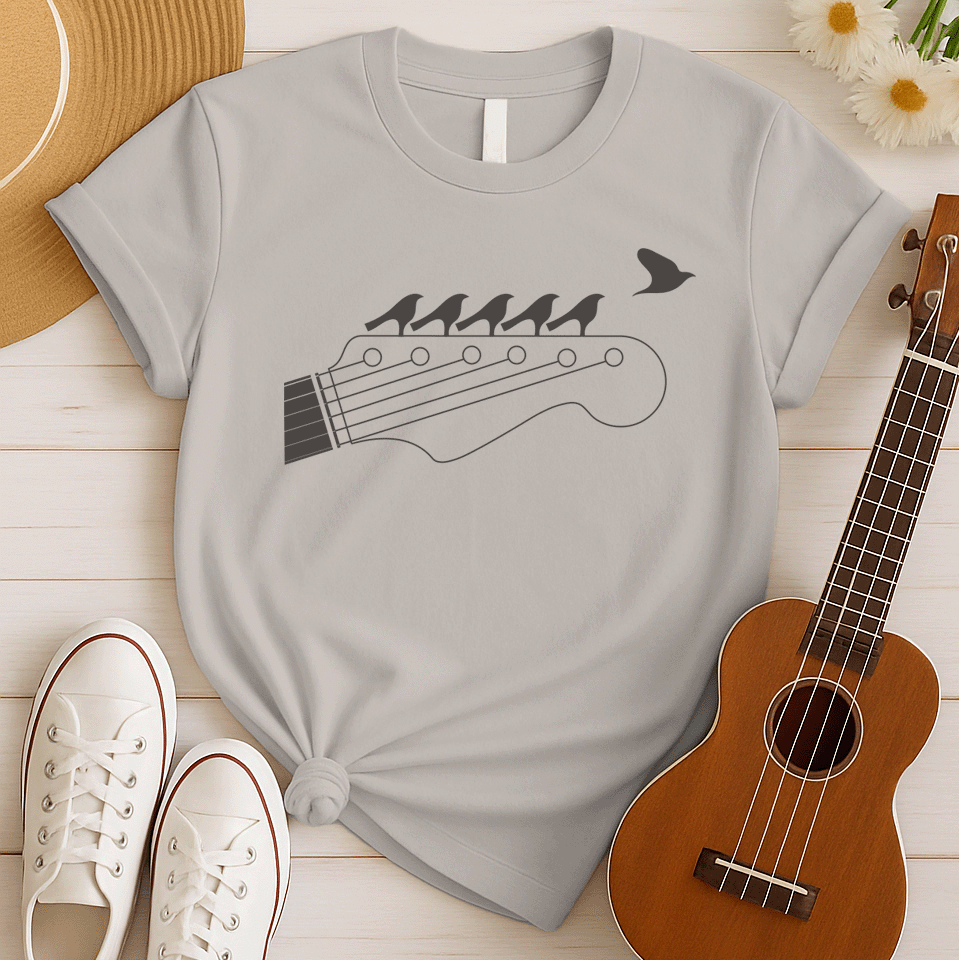 Stylized black graphic of a guitar headstock with tuning pegs and strings. Five small birds are perched in silhouette on the guitar strings, and one bird is depicted flying away in the top right corner. The design suggests musical harmony, freedom, and a connection between nature and guitar music. Ideal for guitar enthusiasts and musicians.