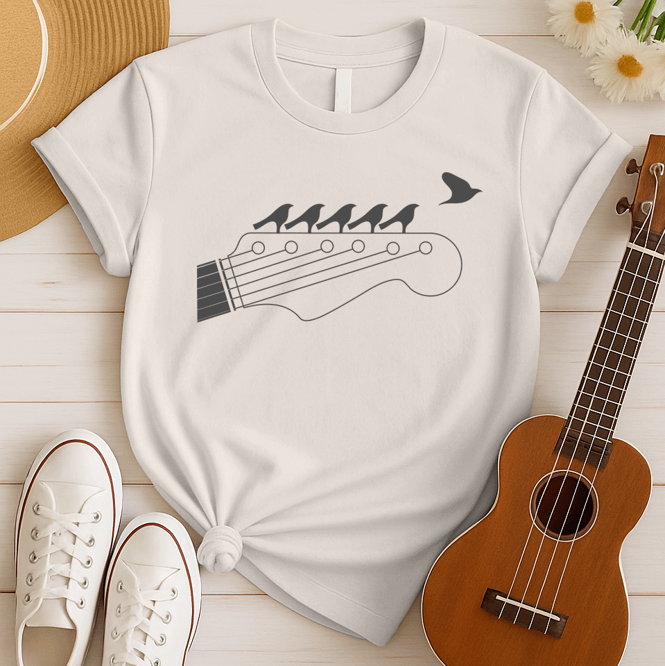 Stylized black graphic of a guitar headstock with tuning pegs and strings. Five small birds are perched in silhouette on the guitar strings, and one bird is depicted flying away in the top right corner. The design suggests musical harmony, freedom, and a connection between nature and guitar music. Ideal for guitar enthusiasts and musicians.