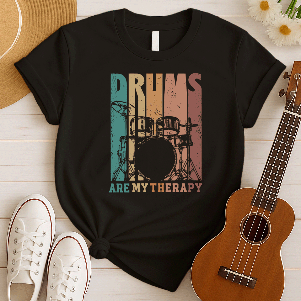 A black background features a stylized drum set (including bass drum, snare, toms, and cymbals) outlined in black. The drum set is filled with distressed vertical stripes of teal, brown, and orange/red. Above the drum set, the text "DRUMS" is in a large, distressed font with similar striped coloring. Below the drum set, the text "ARE MY THERAPY" is prominently displayed in orange. The design expresses a love for drumming, music, and percussion, ideal for drummers and music lovers.