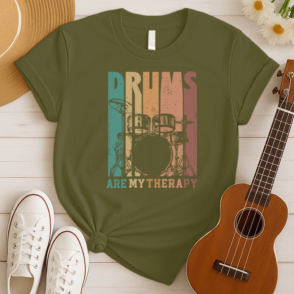 A black background features a stylized drum set (including bass drum, snare, toms, and cymbals) outlined in black. The drum set is filled with distressed vertical stripes of teal, brown, and orange/red. Above the drum set, the text "DRUMS" is in a large, distressed font with similar striped coloring. Below the drum set, the text "ARE MY THERAPY" is prominently displayed in orange. The design expresses a love for drumming, music, and percussion, ideal for drummers and music lovers.