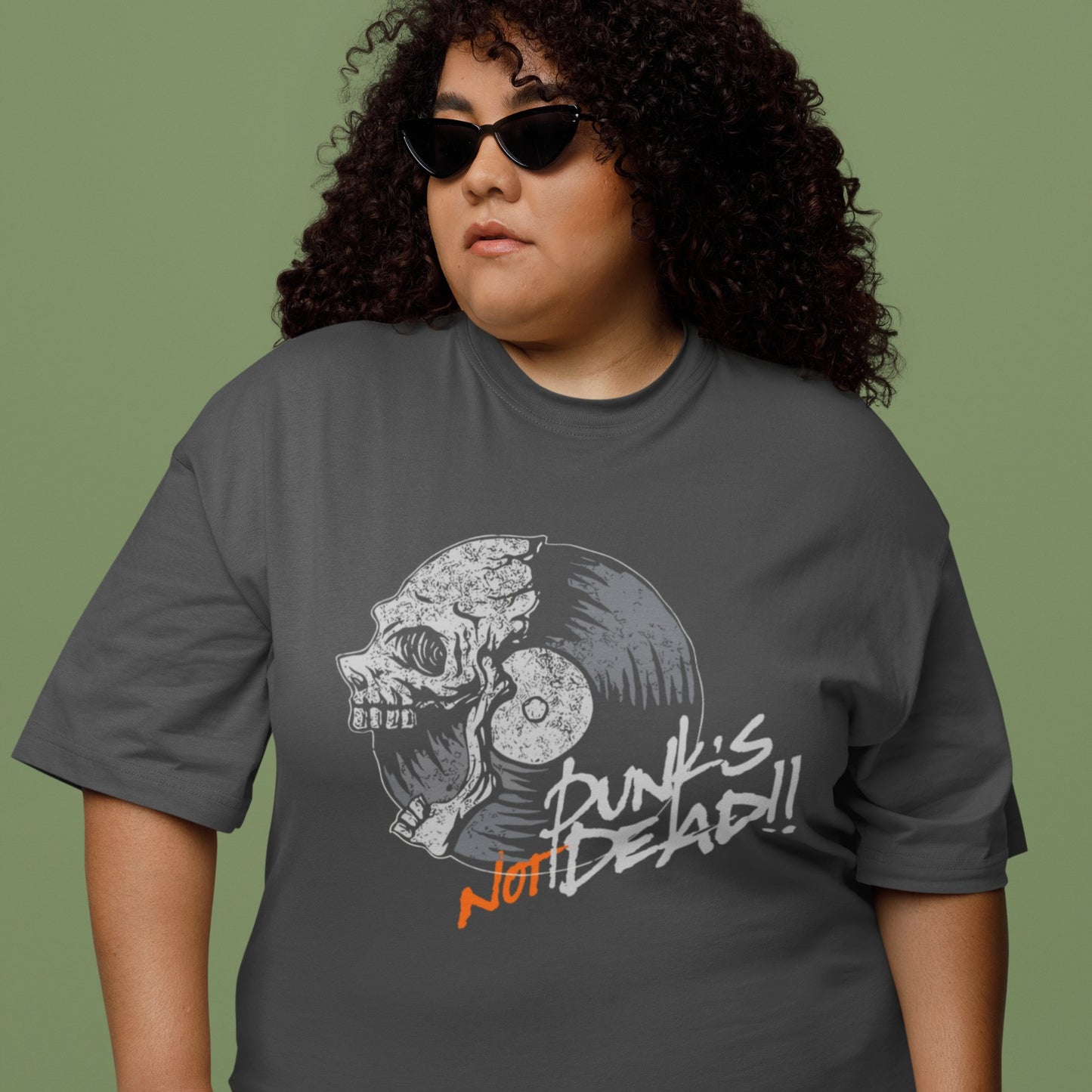 A black background features a stylized illustration of a grey human skull with a crack on its forehead, fused with a vinyl record. The record's grooves and central light grey area are visible. To the right, the distressed grey text reads "Punk's", followed by distressed white text "Not Dead!!". Below this, the orange distressed text "NOT DEAD!!" provides emphasis. The design combines punk music themes with skull imagery and vinyl records.