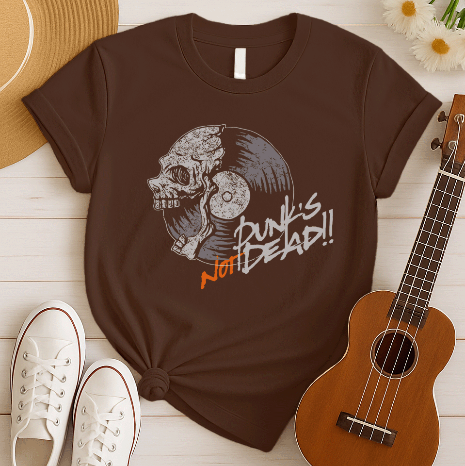 A black background features a stylized illustration of a grey human skull with a crack on its forehead, fused with a vinyl record. The record's grooves and central light grey area are visible. To the right, the distressed grey text reads "Punk's", followed by distressed white text "Not Dead!!". Below this, the orange distressed text "NOT DEAD!!" provides emphasis. The design combines punk music themes with skull imagery and vinyl records.