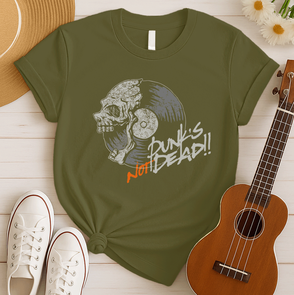 A black background features a stylized illustration of a grey human skull with a crack on its forehead, fused with a vinyl record. The record's grooves and central light grey area are visible. To the right, the distressed grey text reads "Punk's", followed by distressed white text "Not Dead!!". Below this, the orange distressed text "NOT DEAD!!" provides emphasis. The design combines punk music themes with skull imagery and vinyl records.