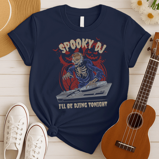 A black background features a stylized illustration of a skeleton with glowing red eyes, wearing headphones and a blue hooded robe, actively operating a DJ turntable. Behind the skeleton, a distressed dark red jack-o'-lantern face and gnarled tree silhouettes are visible. The top text reads "SPOOKY DJ" in distressed orange/brown, and the bottom text in distressed white says "I'LL BE DJING TONIGHT". The design portrays a Halloween-themed DJ ready for a spooky music party.