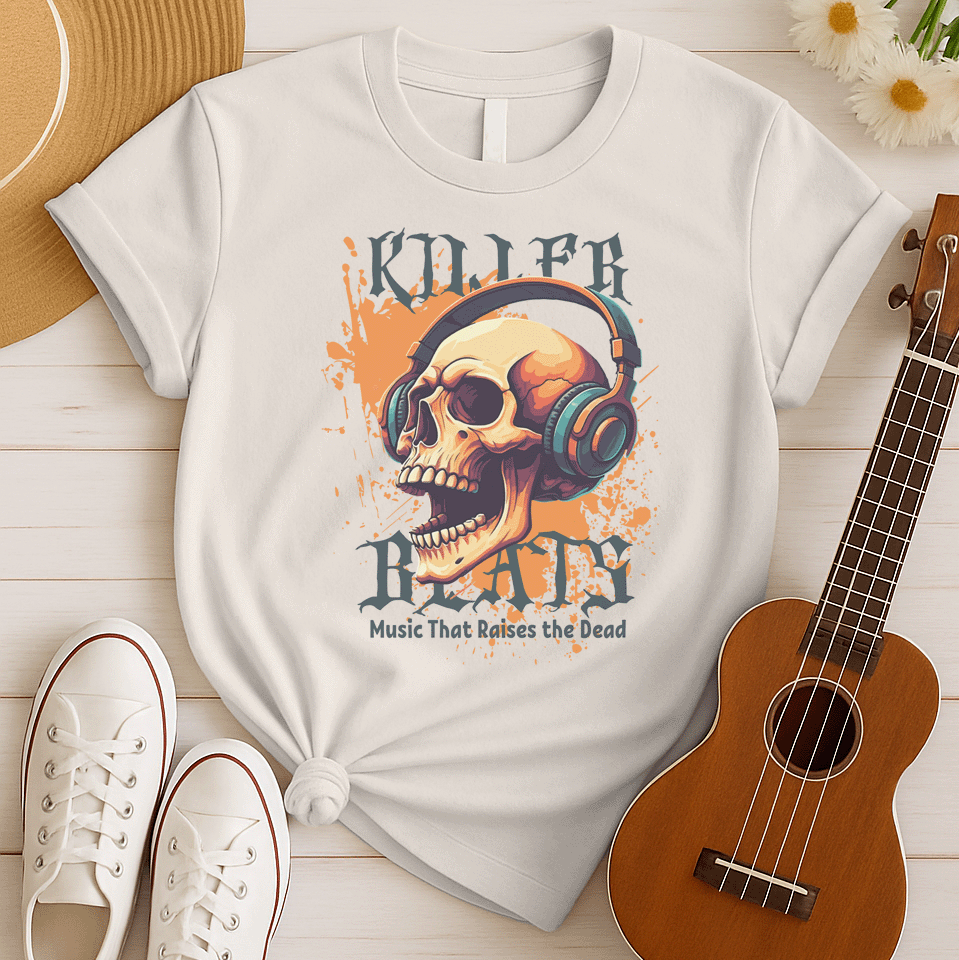 A light grey background with orange paint splatters features a stylized, detailed, orange and yellow human skull wearing large, teal and blue headphones. Distressed grey text above reads "KILLER" and below, "BEATS". Below that, smaller dark grey text says "Music That Raises the Dead". The design is a bold representation of music power and skull art.