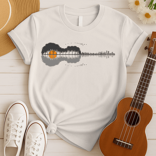 A graphic design features an acoustic guitar silhouette, its body formed by dark gray trees with an orange sun or moon appearing through them. The guitar's neck transitions into a gray sound wave pattern, ending in a minimalist cityscape outline. Flocks of birds fly above and below the design, creating a harmonious blend of nature, music, and urban elements.