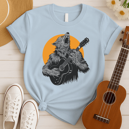 A fierce graphic design showcases a roaring werewolf, rendered in shades of grey and black with piercing orange eyes, powerfully playing an acoustic guitar. The werewolf's head is tilted back, howling, and its sharp teeth and tongue are visible. Behind the creature, a large, vibrant orange circle creates a dramatic backdrop, reminiscent of a full moon or fiery sun. The entire composition conveys a raw, untamed passion for music and a connection to supernatural energy