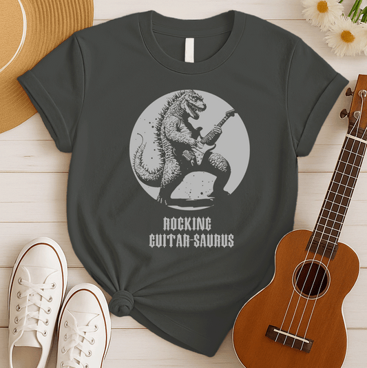A bold, monochromatic graphic design features a fierce, reptilian creature, resembling Godzilla, shredding an electric guitar with intensity. The creature is silhouetted in black against a light grey circular background, which gives the impression of a full moon or spotlight. Below the image, the text "ROCKING GUITAR-SAURUS" is displayed in a stylized, jagged font, all set against a solid black background. The design combines the power of a dinosaur with the energy of rock and roll.