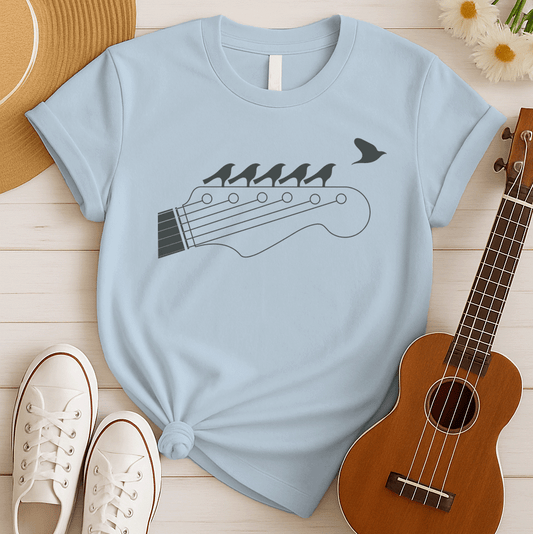 Stylized black graphic of a guitar headstock with tuning pegs and strings. Five small birds are perched in silhouette on the guitar strings, and one bird is depicted flying away in the top right corner. The design suggests musical harmony, freedom, and a connection between nature and guitar music. Ideal for guitar enthusiasts and musicians.
