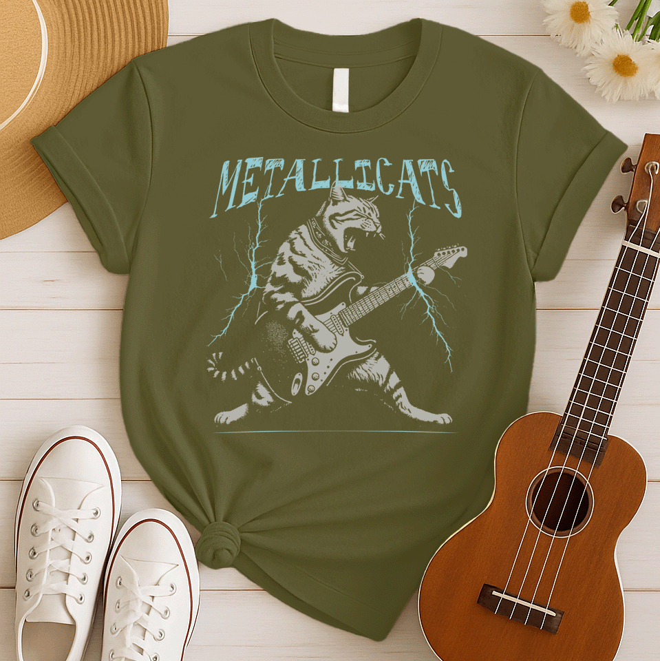 Dynamic graphic of a gray striped tabby cat with its mouth open, appearing to roar, passionately playing a black and white electric guitar. Blue lightning bolts emanate from the guitar. Text above reads "METALLICATS". The cat wears a studded collar. Ideal for heavy metal fans, rock music lovers, guitarists, and cat lovers.
