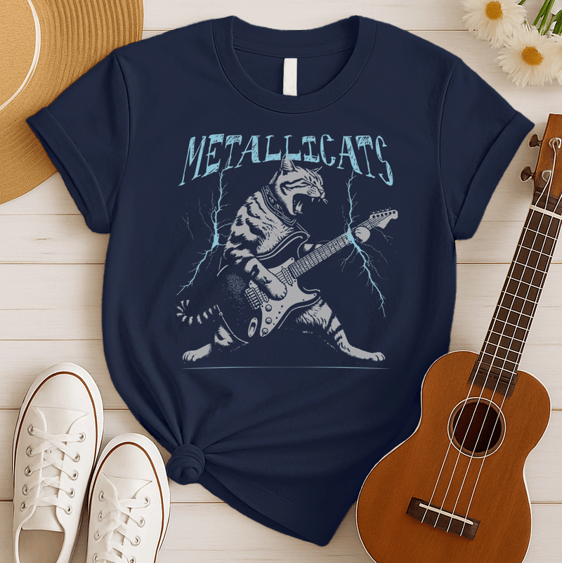 Dynamic graphic of a gray striped tabby cat with its mouth open, appearing to roar, passionately playing a black and white electric guitar. Blue lightning bolts emanate from the guitar. Text above reads "METALLICATS". The cat wears a studded collar. Ideal for heavy metal fans, rock music lovers, guitarists, and cat lovers.