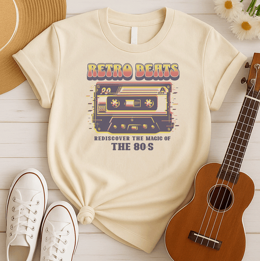 Stylized graphic of a classic audio cassette tape in red, yellow, and blue colors with a glitch effect. Large, distressed orange text above reads "RETRO BEATS". Smaller orange text below reads "REDISCOVER THE MAGIC OF THE 80S". The design evokes vintage music, 80s pop culture, and retro audio technology. Ideal for 80s enthusiasts and music lovers.