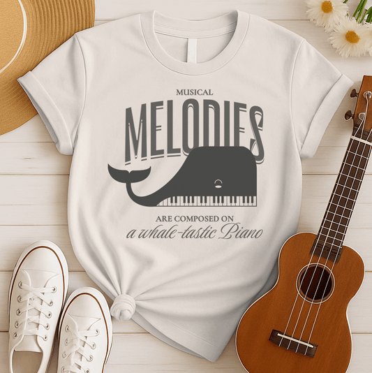 Stylized graphic of a dark gray whale with a piano keyboard forming its lower jaw/body. Grey text above reads "MUSICAL MELODIES" and smaller text below reads "ARE COMPOSED ON a whale-tastic Piano". The design is whimsical, combining music, a piano instrument, and a whale, ideal for music lovers, pianists, and marine life enthusiasts.