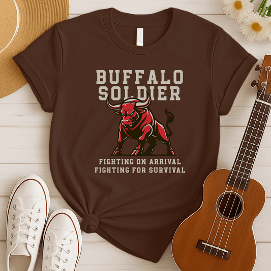 A striking graphic design features a powerfully built red bull with menacing green eyes and prominent horns, depicted in a charging or aggressive stance. The bull's body is outlined in a lighter shade of red, giving it depth. Above the bull, the words "BUFFALO SOLDIER" are written in bold, athletic-style block letters, with "BUFFALO" in white and "SOLDIER" in light grey. Below the bull, two lines of text read "FIGHTING ON ARRIVAL" and "FIGHTING FOR SURVIVAL," both in white, bold, block letters.