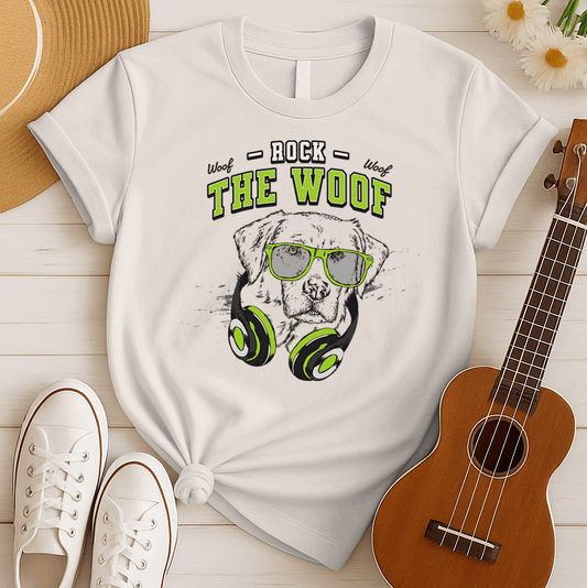 Graphic of a black dog's head wearing bright green-rimmed sunglasses and large headphones with green accents. White distressed text above reads "ROCK" and below the dog's head, large green text with a black outline reads "THE WOOF". Smaller "Woof" texts are on either side of "ROCK". The design suggests rock music, dog lovers, and a cool animal DJ aesthetic. Ideal for pet owners and music enthusiasts.