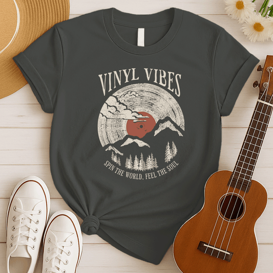 Stylized graphic of a large vinyl record serving as a mountainous landscape, with trees and clouds. The record label is reddish-brown. White distressed text above reads "VINYL VIBES". Curved white text below reads "SPIN THE WORLD, FEEL THE SOUL". The design evokes vintage music, nature, and meditative vibes, ideal for vinyl collectors and music lovers.