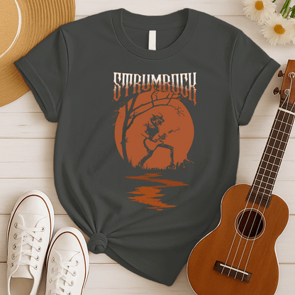 Stylized graphic of a silhouetted guitarist in a hat and jacket, passionately playing an acoustic or electric guitar against a large, glowing orange full moon. A bare tree branch extends over them. Orange text above reads "STRUMROCK". The scene evokes a rock concert or solo performance under the night sky, ideal for guitar players, rock music fans, and musicians.