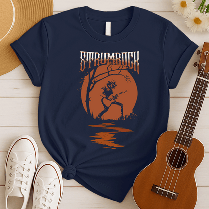 Stylized graphic of a silhouetted guitarist in a hat and jacket, passionately playing an acoustic or electric guitar against a large, glowing orange full moon. A bare tree branch extends over them. Orange text above reads "STRUMROCK". The scene evokes a rock concert or solo performance under the night sky, ideal for guitar players, rock music fans, and musicians.