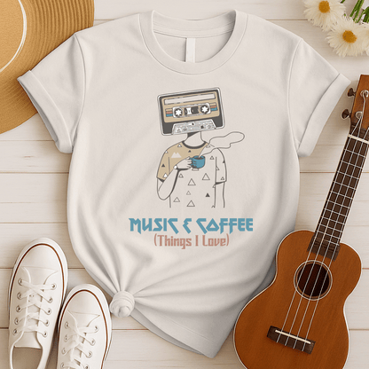 Stylized graphic of a person's body with a vintage brown and black audio cassette tape as its head, holding a blue steaming coffee cup. Small triangle patterns are on the person's beige shirt. Blue distressed text below reads "MUSIC & COFFEE" and red text below that says "(Things I Love)". The design embodies music appreciation, coffee love, and retro nostalgia, ideal for music lovers and coffee enthusiasts.