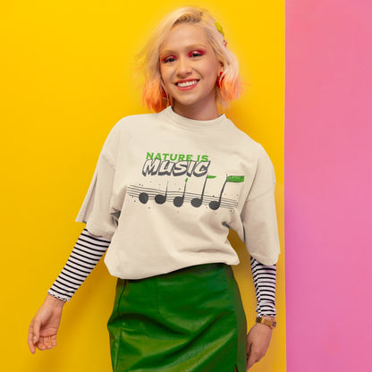 A tshirt design features the text "NATURE IS" in a distressed green font at the top. Below it, the word "MUSIC" is prominently displayed in a larger, distressed dark grey font with a subtle 3D effect. Below the text, a horizontal musical staff is shown with five round, dark grey quarter notes. Each note has a small green leaf growing from its stem, with the last note having a larger, more prominent green leaf. The design symbolizes the connection between nature and music, perfect for environmentalists an