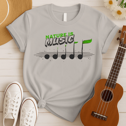 A tshirt design features the text "NATURE IS" in a distressed green font at the top. Below it, the word "MUSIC" is prominently displayed in a larger, distressed dark grey font with a subtle 3D effect. Below the text, a horizontal musical staff is shown with five round, dark grey quarter notes. Each note has a small green leaf growing from its stem, with the last note having a larger, more prominent green leaf. The design symbolizes the connection between nature and music, perfect for environmentalists an