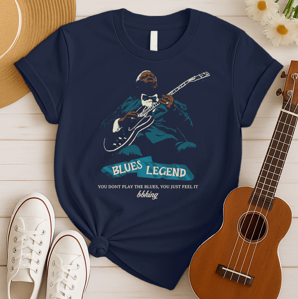 A black background features a stylized, silhouette-like illustration of a dark-skinned man in a suit and bow tie, playing an electric guitar. Highlights on his face, hands, guitar, and suit are in light brown/white and teal. Below the figure, two distressed, light blue shapes contain the text "BLUES LEGEND". Further below, the distressed white text reads "YOU DONT PLAY THE BLUES, YOU JUST FEEL IT", followed by "bbking" in a distressed, handwritten-style font. The design is a powerful tribute to blues music 