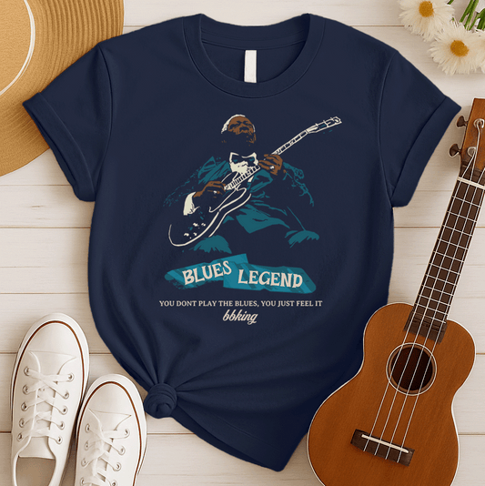 A black background features a stylized, silhouette-like illustration of a dark-skinned man in a suit and bow tie, playing an electric guitar. Highlights on his face, hands, guitar, and suit are in light brown/white and teal. Below the figure, two distressed, light blue shapes contain the text "BLUES LEGEND". Further below, the distressed white text reads "YOU DONT PLAY THE BLUES, YOU JUST FEEL IT", followed by "bbking" in a distressed, handwritten-style font. The design is a powerful tribute to blues music 