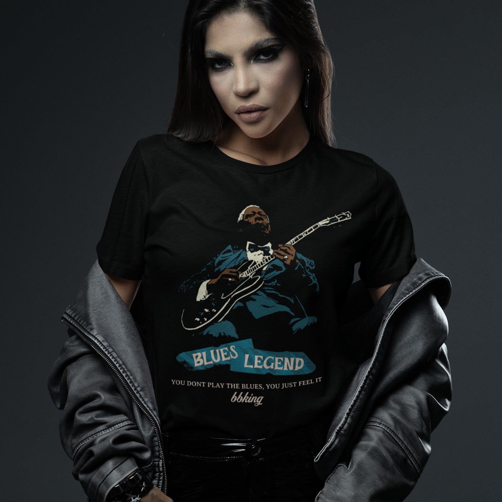 A black background features a stylized, silhouette-like illustration of a dark-skinned man in a suit and bow tie, playing an electric guitar. Highlights on his face, hands, guitar, and suit are in light brown/white and teal. Below the figure, two distressed, light blue shapes contain the text "BLUES LEGEND". Further below, the distressed white text reads "YOU DONT PLAY THE BLUES, YOU JUST FEEL IT", followed by "bbking" in a distressed, handwritten-style font. The design is a powerful tribute to blues music 