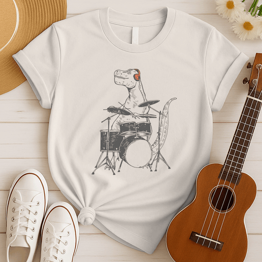 A fun and unique graphic features a dark grey Tyrannosaurus Rex (T-Rex) wearing bright orange headphones and playing a full drum kit. The T-Rex is depicted mid-action, with drumsticks in its small hands, actively hitting the drums and cymbals. The drum kit elements, including the bass drum, snare, and cymbals, are also rendered in shades of grey. This humorous illustration, cleverly combines prehistoric power with musical rhythm.